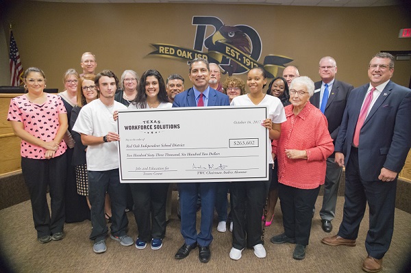 Group of folks in business and business casual attire holding a large check from Workforce Solutions.